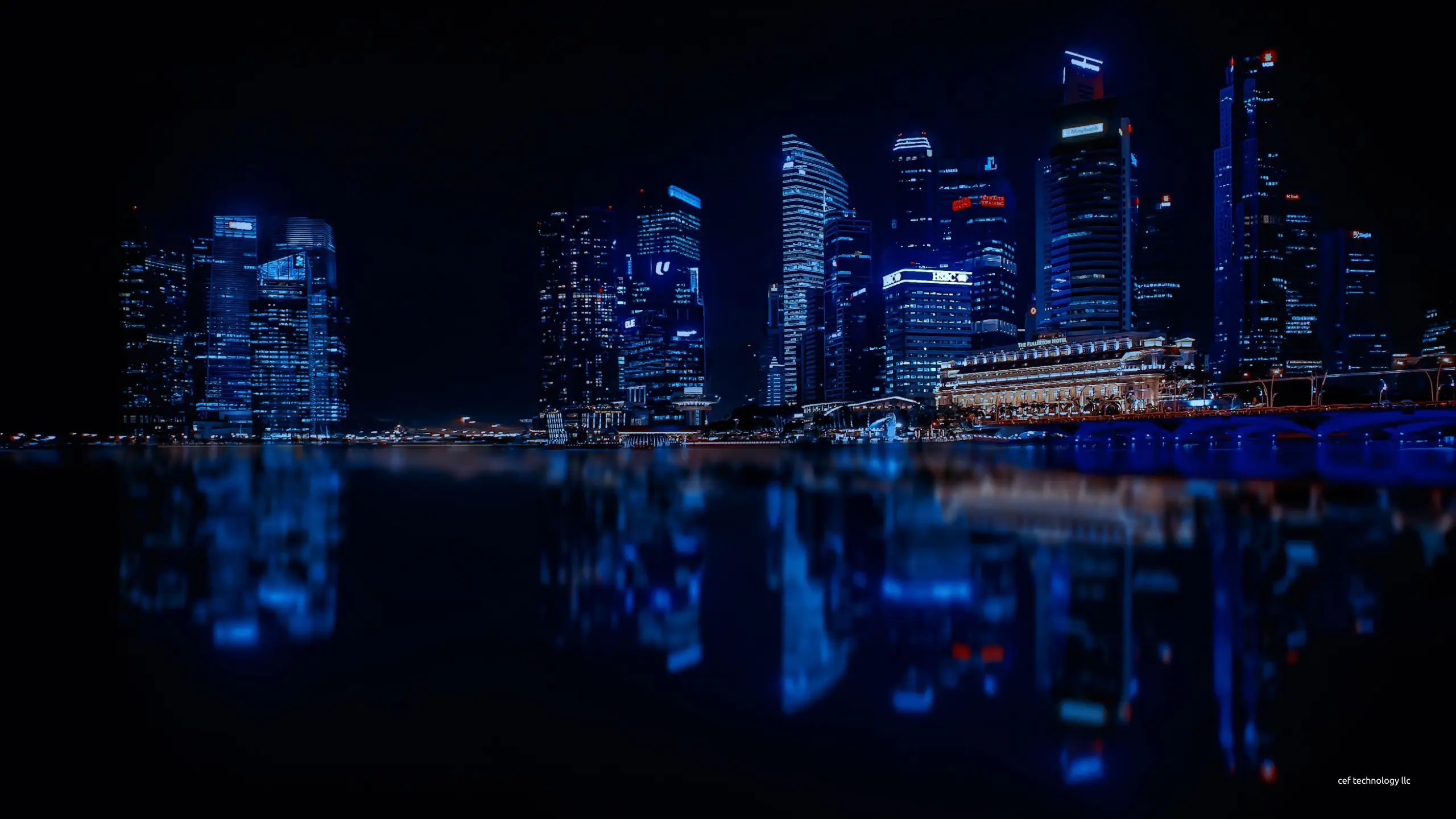 A financial district skyline at night, its lit towers reflected in the water.